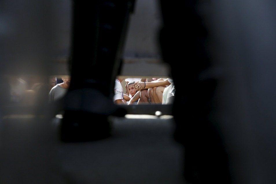 Inmates are seen sitting down, under a gate and through the legs of a police officer at the National Bolivarian Police prison, during a riot in Caracas, Venezuela