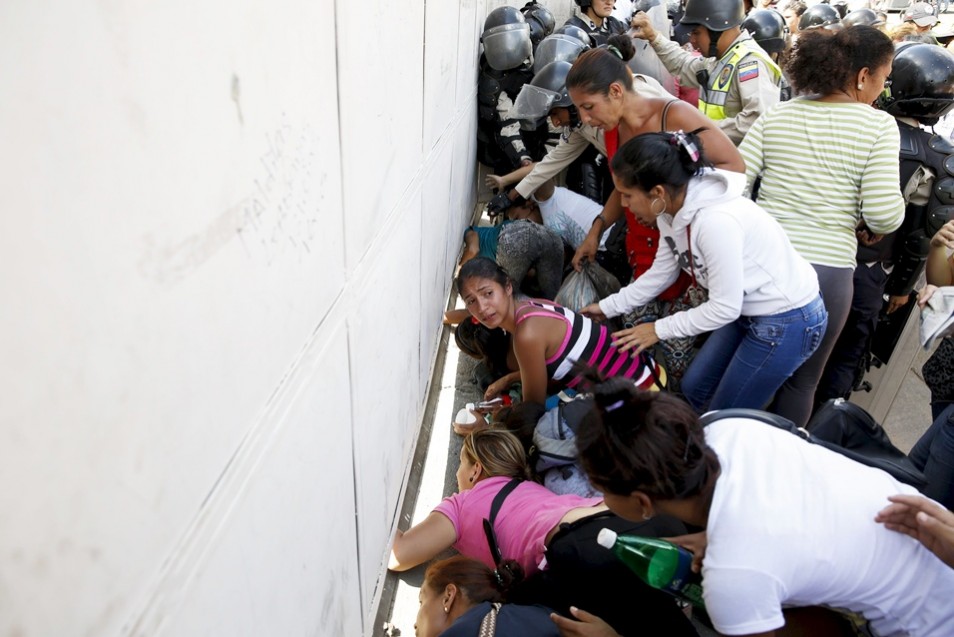 Relatives of inmates react as they try to look inside the National Bolivarian Police prison under a gate, during a prison riot in Caraca